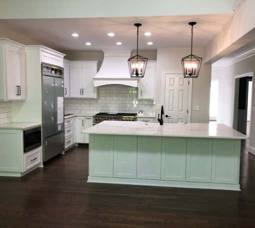 Modern kitchen with white cabinets, stainless steel appliances, a large island with a white countertop, pendant lights, and dark wood flooring.