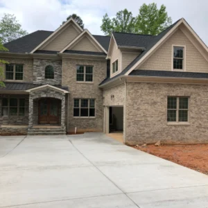 Two-story brick house with a double front door, attached garage, multiple windows, and a large concrete driveway.